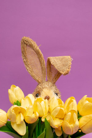 Bunny rabbit ears made of natural plants material with yellow tulips on purple background. Easter...