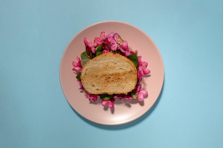 Sandwich with pink spring flowers on blue background with copy space.