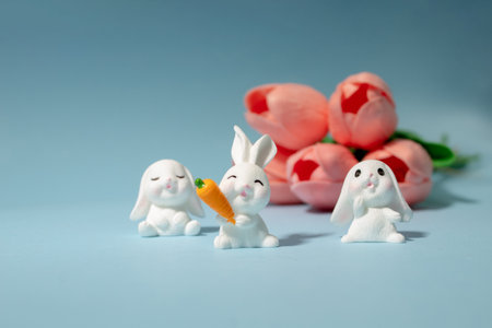 Miniature white bunnies with carrot and pink tulips with blue background. Easter spring concept.の写真素材