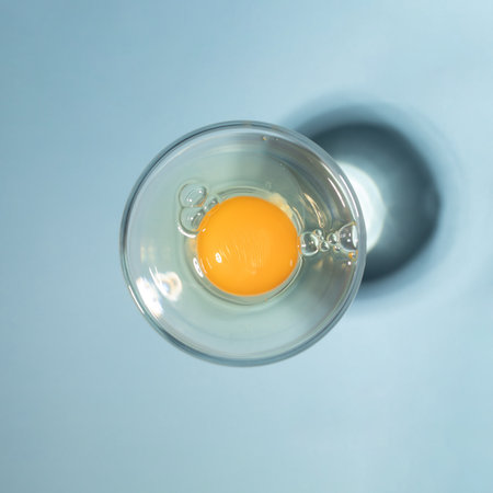 Raw egg in the glass on pastel blue background. Sunny day concept. Flat layの写真素材