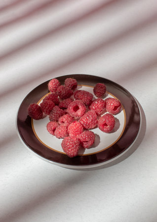 Fresh raspberries on a plate on the table with shadowon light background. Food photographyの写真素材