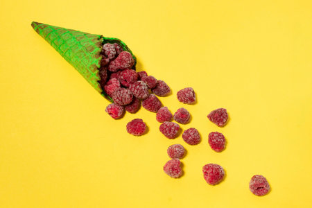 Frozen raspberries in green ice cream cone, on yellow background. Vibrant food photography. Flat layの写真素材
