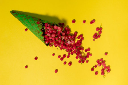 Red currants in a green ice cream cone on a yellow background. Vibrant food photography
