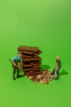Miniature people makes a chocolate biscuit with a shovel on green background.の写真素材