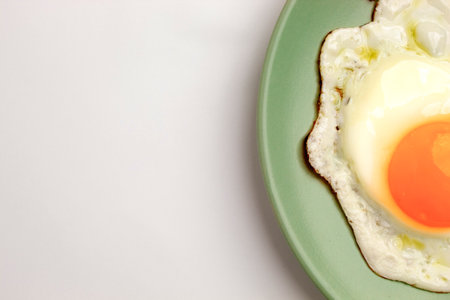 A fried egg on a pastel green plate on a pastel purple background. Close-up