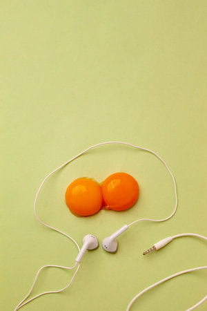 Egg made of double raw egg yolks and white headphone cable on pastel green background. Flat lay....