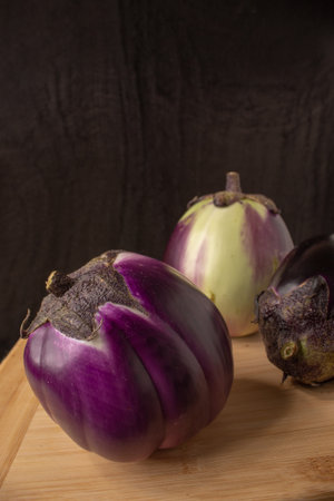 Eggplants on a wooden kitchen table with black background. Still lifeの写真素材