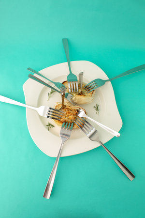 Roasted white eggplant on a white plate on a vibrant blue background with forks stuck in it. Creative composition of contemporary foodの写真素材