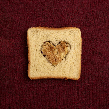 Toast bread with shape of heart on burgundy background, top view