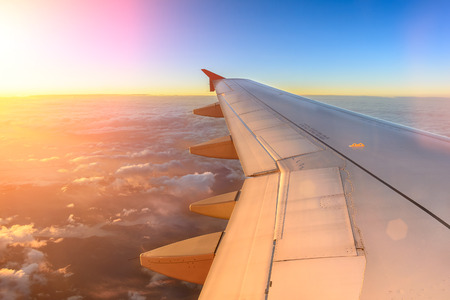 Aerial view of airplane flying above shade clouds and sky from an airplane fly during the sunset. View from the plane window of emotional moment during international travel around the world.