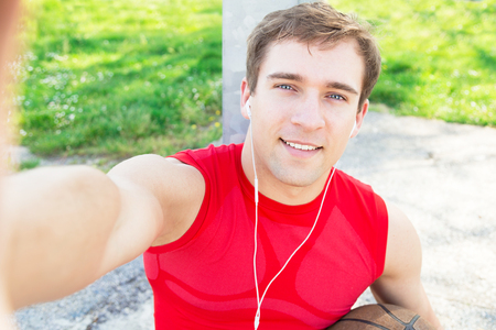 Sitting guy in a basketball court and take a selfie after match with friends - listen music with headphones - Blond man finish to do sport and make himself pictureの写真素材