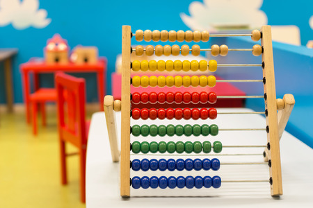 Educational toy for babies inside colorful room with red chairs and blue wall - Multicolor wooden abacus on the white desk - Concept of education learning and teaching - Main focus on red ballsの写真素材