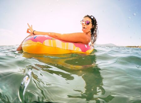 Young Girl Relaxing and Enjoying on her Vacation Holiday Trip at the Ocean with a Inflatable Donut Lilo Float Ring. Wanderlust Woman Spending Time Outdoors at the Tropical Sea. Summer Holiday Concept.の写真素材