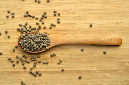 Many dried okra seeds in wooden spoon, on bamboo cutting boardの写真素材