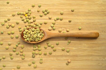 Dry green lentil grains in wooden spoon, on bamboo cutting board
