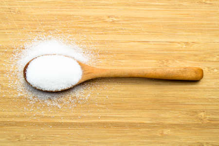 White granulated sugar in wooden spoon on bamboo cutting board, on bamboo cutting boardの写真素材