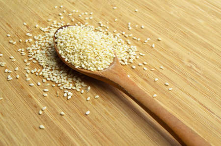 Organic fresh raw sesame seeds, in wooden spoon on bamboo cutting boardの写真素材