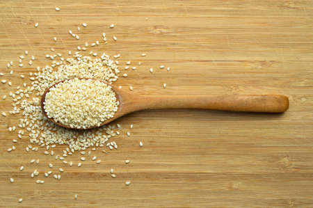 Organic fresh raw sesame seeds, in wooden spoon on bamboo cutting boardの写真素材
