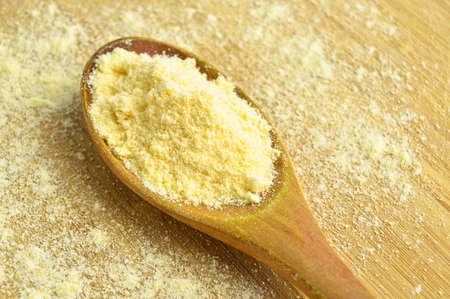 Uncooked yellow corn flour in wooden spoon on bamboo cutting board