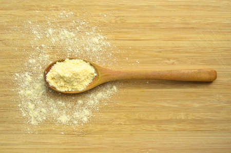 Uncooked yellow corn flour in wooden spoon on bamboo cutting board