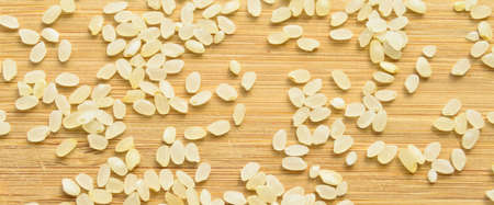 Fresh organic white raw dried rice grains texture, on bamboo cutting board