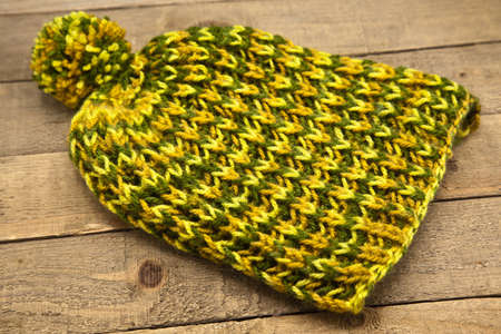 Handmade wool knitted winter yellow and green, hat isolated on wooden background
