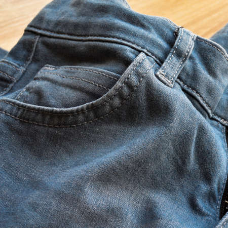 Close up detail of pocket of light blue jeans denim, on wooden floor