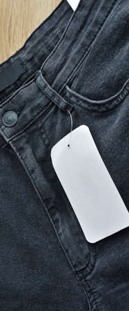 Zipper pocket and buttons black jeans denim and blank sale tag paper, on wooden floor