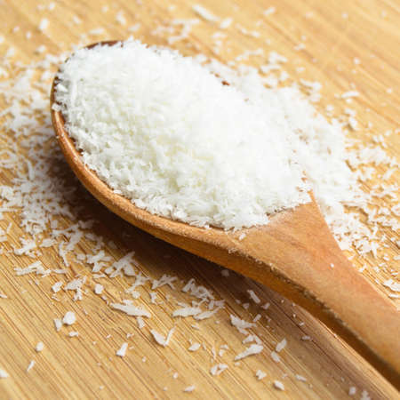 Ground fresh and nutritious coconut in wooden spoon on bamboo cutting boardの写真素材