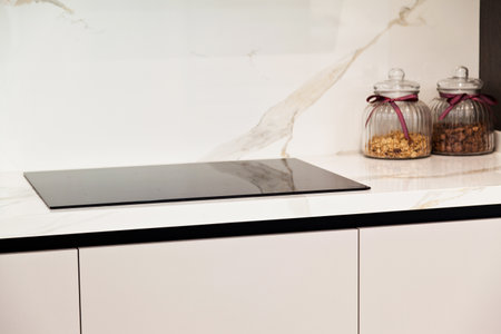 Modern gray white lacquer wood kitchen cabinet equipment and black electric stove on white granite countertop in homeの写真素材