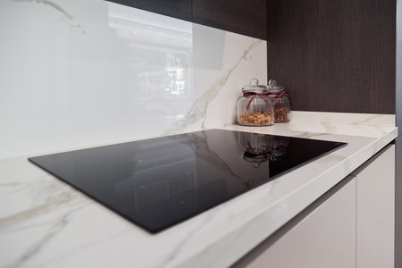 Modern gray white lacquer wood kitchen cabinet equipment and black electric stove on white granite countertop in homeの写真素材
