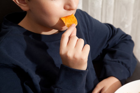 Caucasian person in navy blue t-shirt eating potato chips with appetite and pleasure, young male, man child eating potato chipsの写真素材