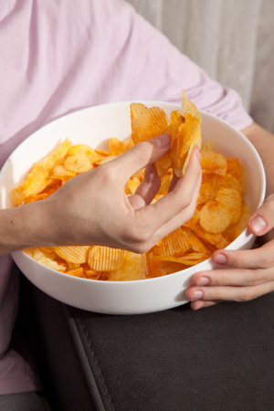 Caucasian person in pink t-shirt holding white plate full of potato chips and preparing to eat