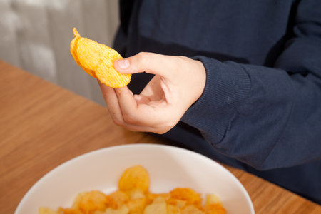 Caucasian person in navy blue t-shirt holding white plate full of potato chips and preparing to eat