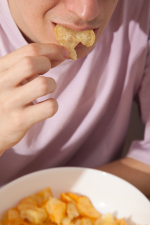 Caucasian person in pink t-shirt holding white plate full of potato chips, young male eating potato chipsの写真素材