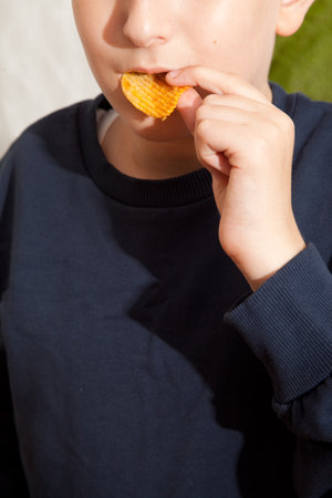 Caucasian person in navy blue t-shirt eating potato chips with appetite and pleasure, young male, man child eating potato chipsの写真素材