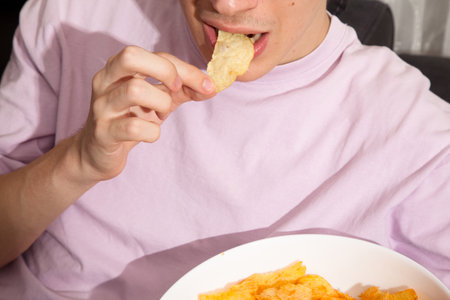 Caucasian person in pink t-shirt holding white plate full of potato chips, young male eating potato chipsの写真素材