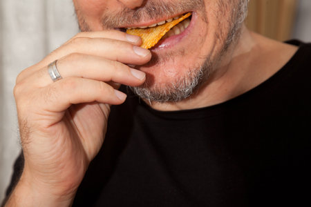 Caucasian person in black t-shirt eating potato chips with appetite and pleasure, middle-aged...