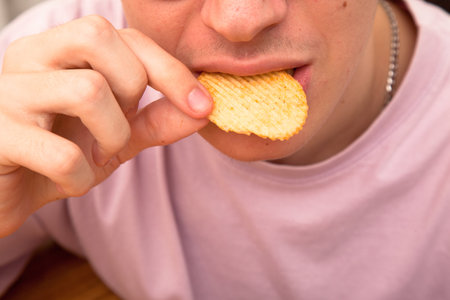 Caucasian person in pink t-shirt eating potato chips with appetite and pleasure, young male eating potato chipsの写真素材