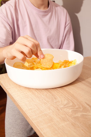Caucasian person in pink t-shirt holding white plate full of potato chips and preparing to eat