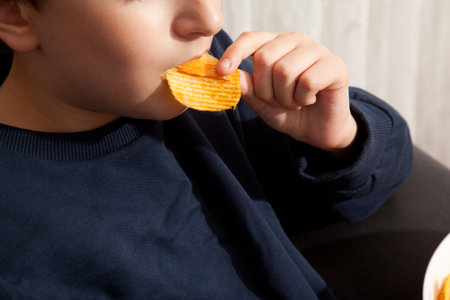 Caucasian person in navy blue t-shirt eating potato chips with appetite and pleasure, young male, man child eating potato chipsの写真素材