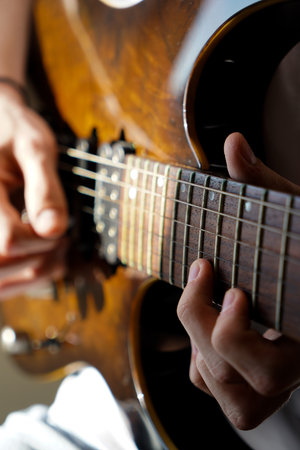 Hands of a Caucasian musician playing electric guitar, playing bright brown color wooden electric...