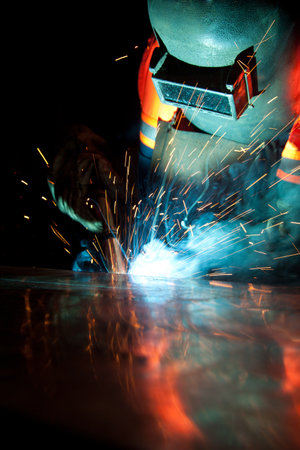 Welder uses torch to make sparks during manufacture of metal equipment, industrial professional...