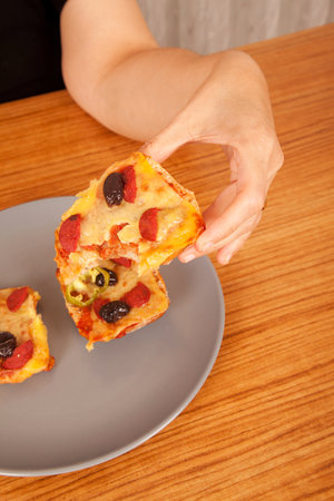 Person holding delicious pizza slices in gray plate on brown wooden table
