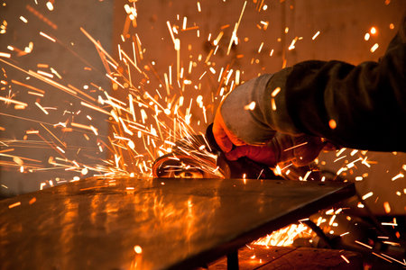 A worker working in a heavy industry or factory is holding a cutting stone or grinding stone and...