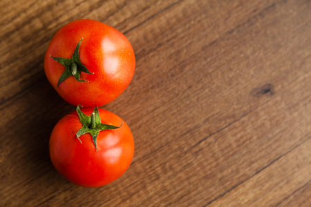 Fresh, tasty organic vegetables, shiny two red tomatoes, isolated on brown wood cutting boardの写真素材