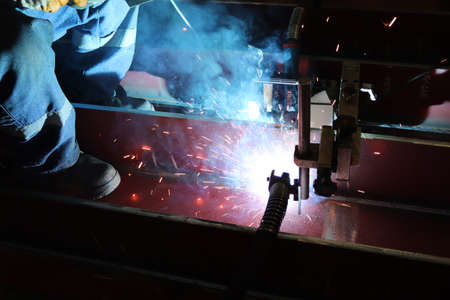 The welder is welding the steel with an electric welding machine inside the factory.