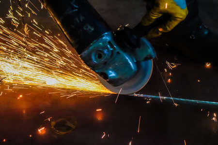 Industrial worker using angle grinder to cut metal. Sparks while grinding iron