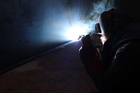 Welder in protective mask welding metal at construction site. Sparks from welding machine.