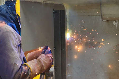 Industrial worker with protective mask welding metal in factory. Sparks from welding machine.